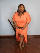 Plus size coral wrap midi dress with waist tie and high low hem styled with heels