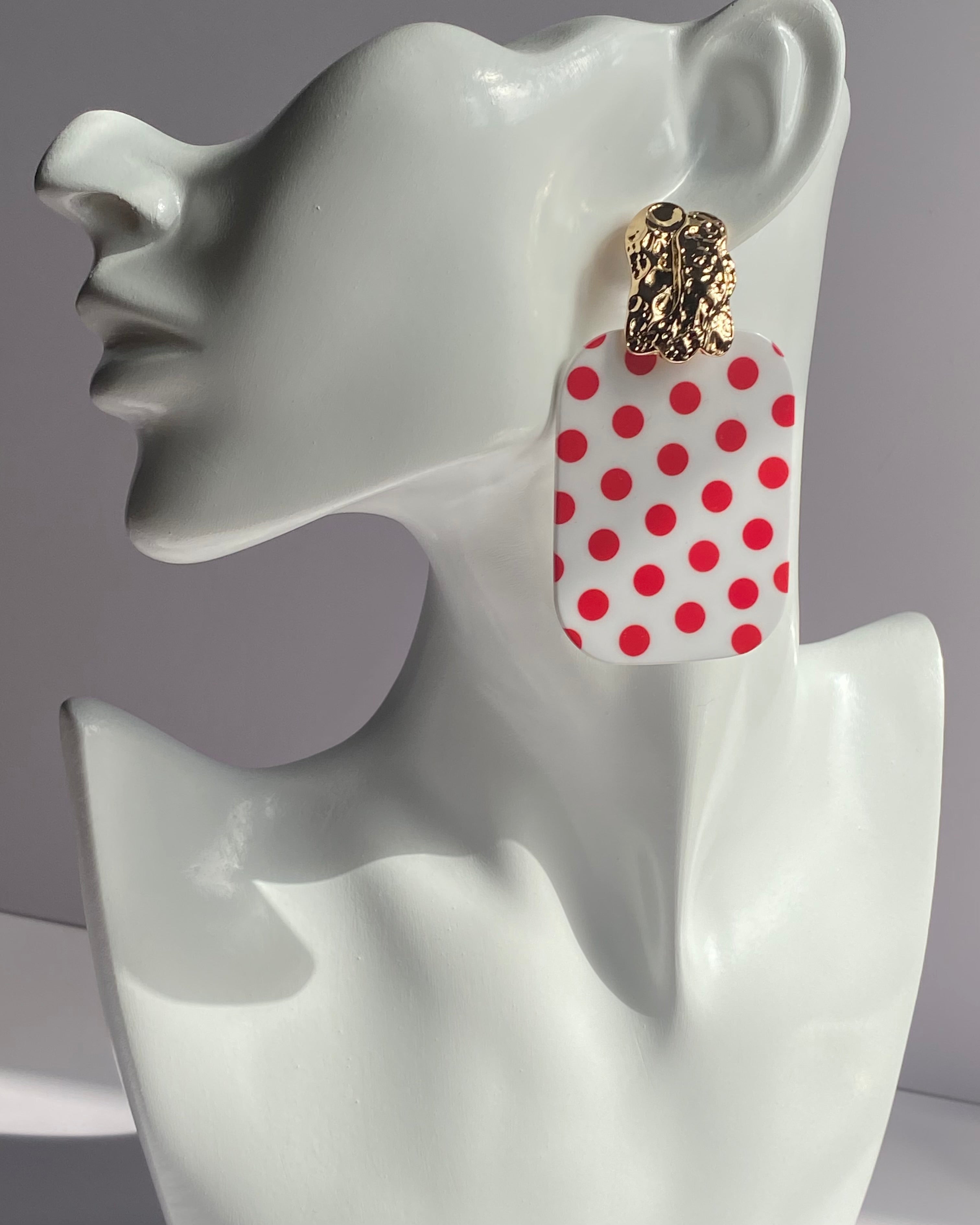 White acrylic polka dot statement earrings with gold-tone textured studs available in red and black variations.