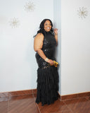 Woman wearing black sequin evening gown with layered chiffon skirt and gold heels