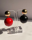 Gold ball drop statement earrings with glossy red and black sphere variations and polished gold-tone studs.
