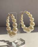 Graduated ivory pearl hoop earrings with gold-tone hardware displayed on a clear acrylic stand.