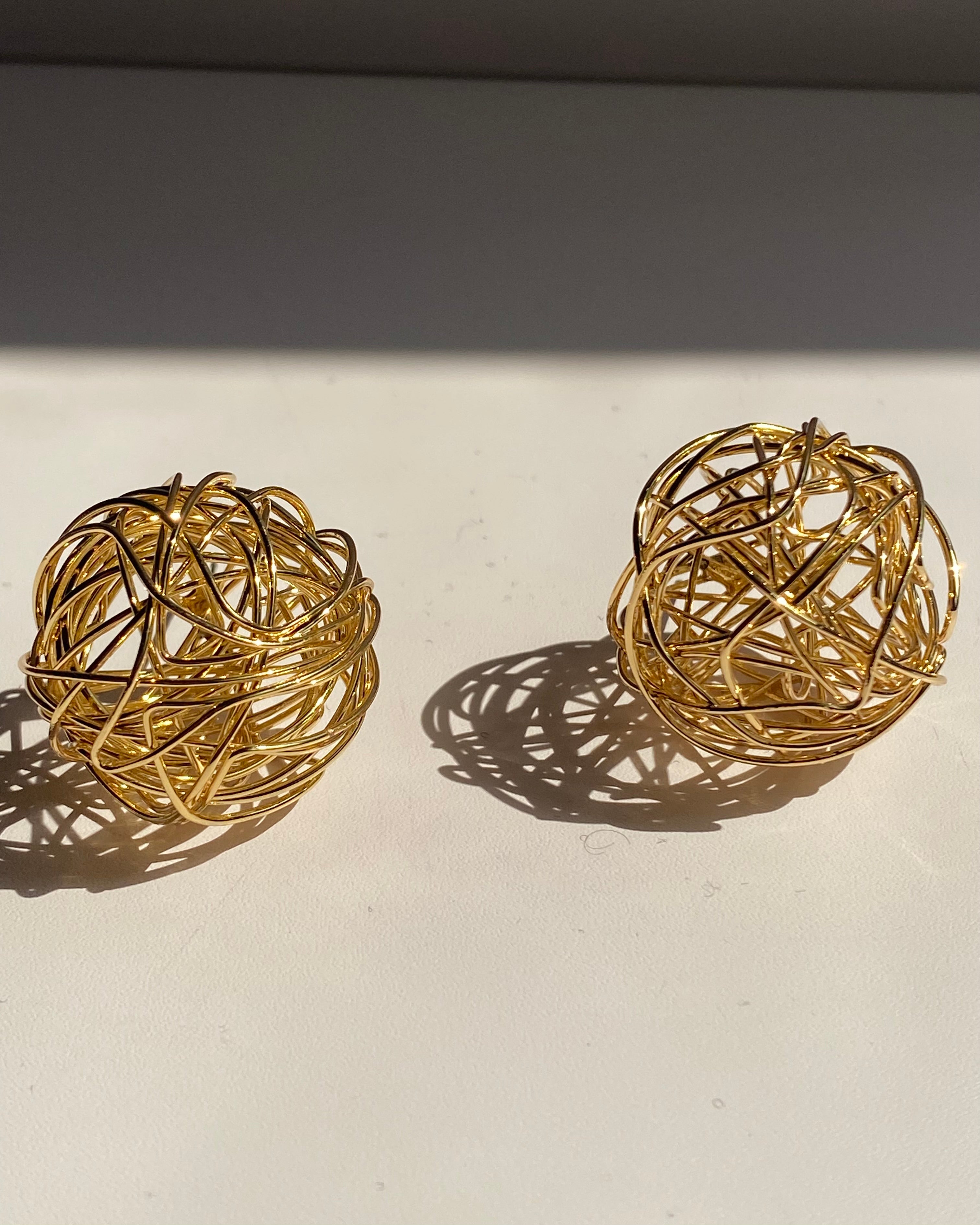Interwoven orb statement earrings in gold and silver finishes.