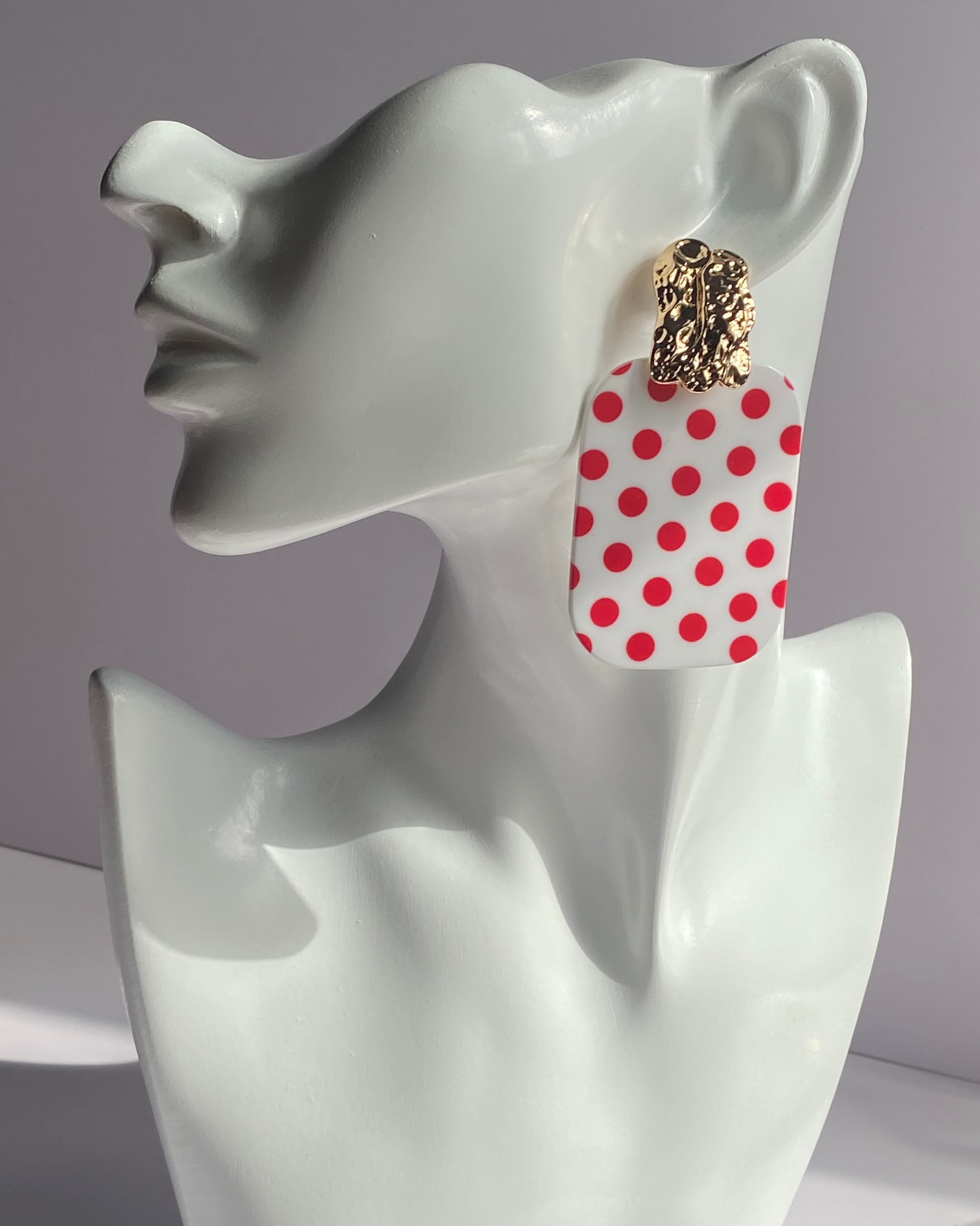 White acrylic polka dot statement earrings with gold-tone textured studs available in red and black variations.
