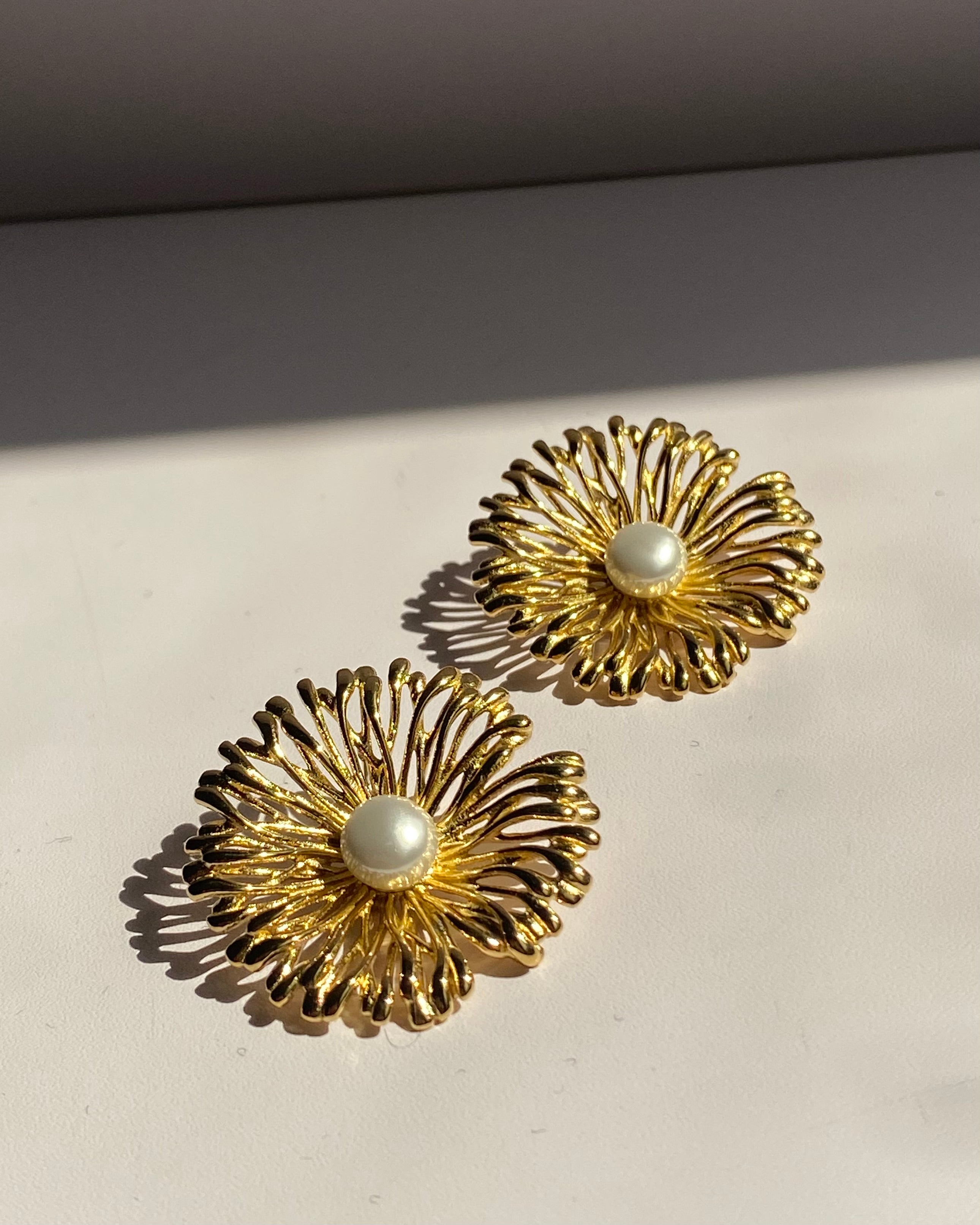 Pearl center sunburst stainless steel stud earrings available in gold and silver finishes.