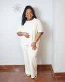 Plus size model wearing an oatmeal scuba knit matching set with a curved hem top and wide leg pants.