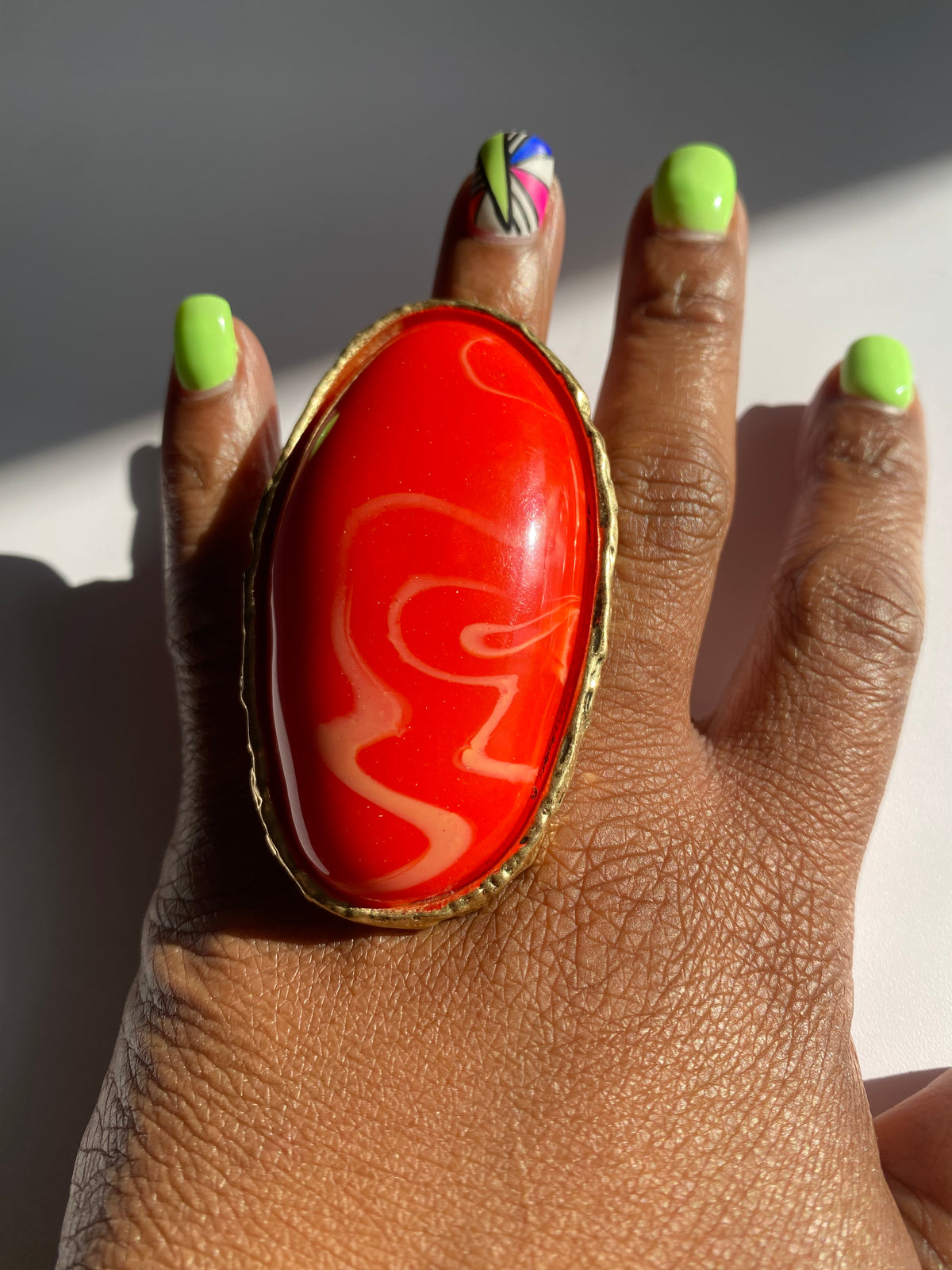Oversized coral red resin statement ring with textured gold-tone frame and adjustable band.