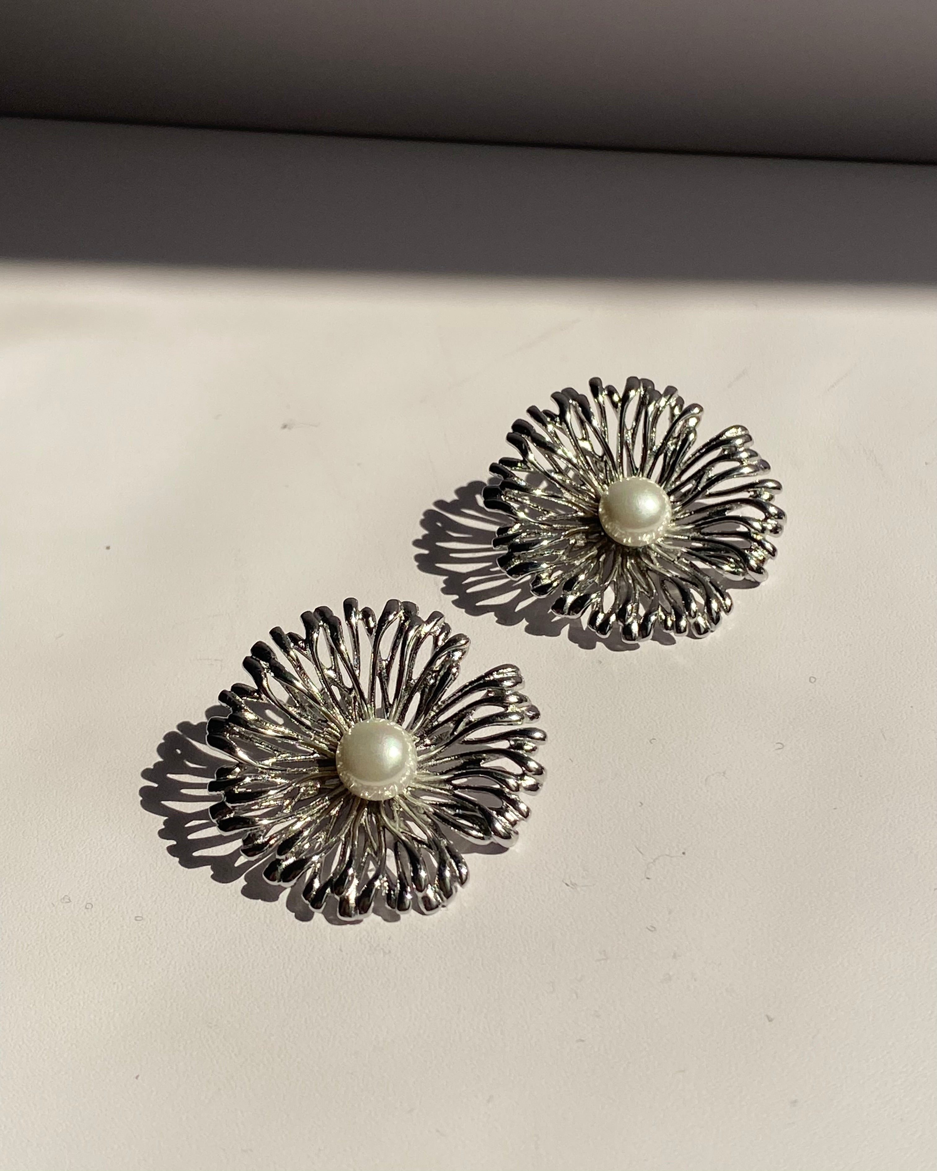 Pearl center sunburst stainless steel stud earrings available in gold and silver finishes.