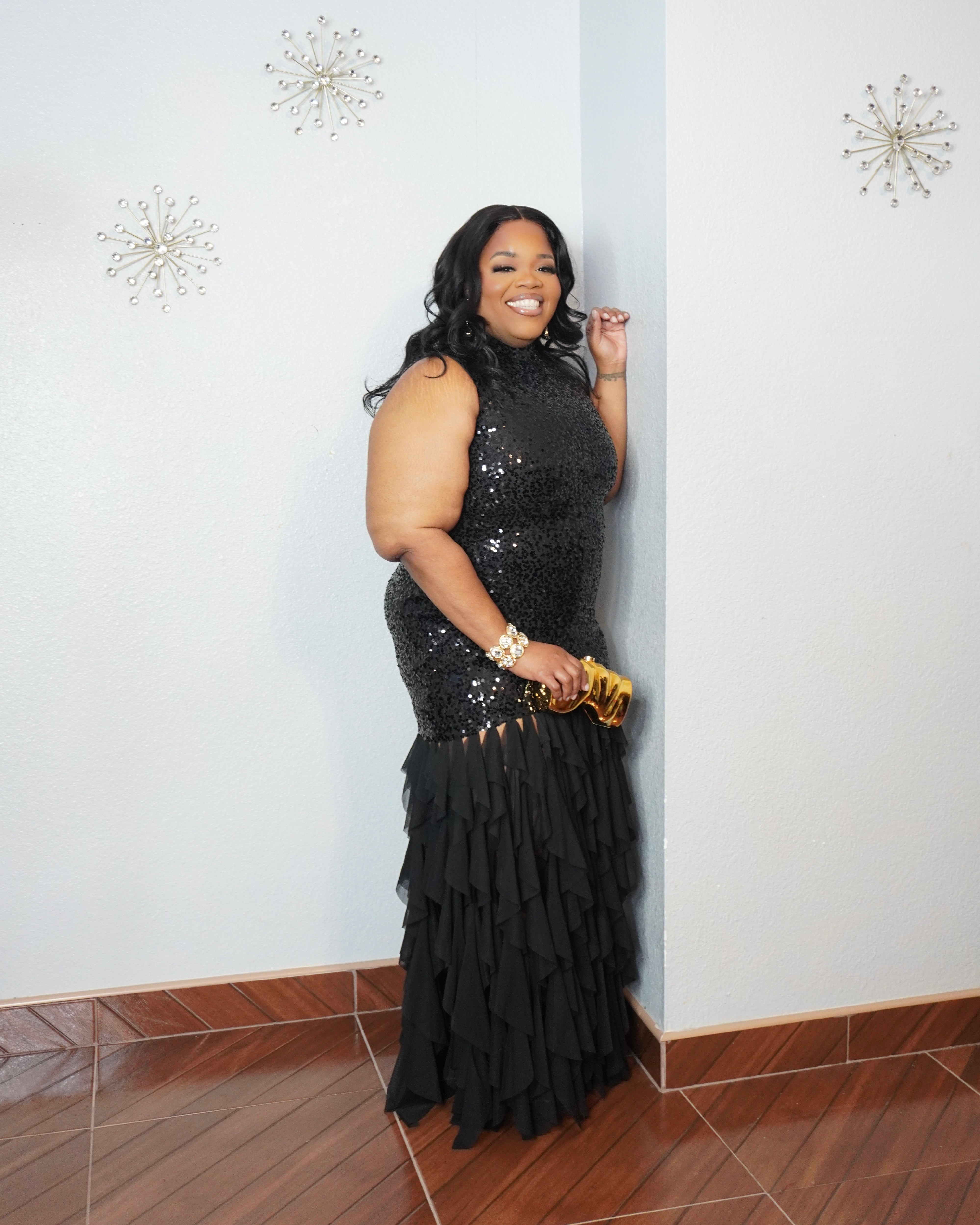 Woman wearing black sequin evening gown with layered chiffon skirt and gold heels
