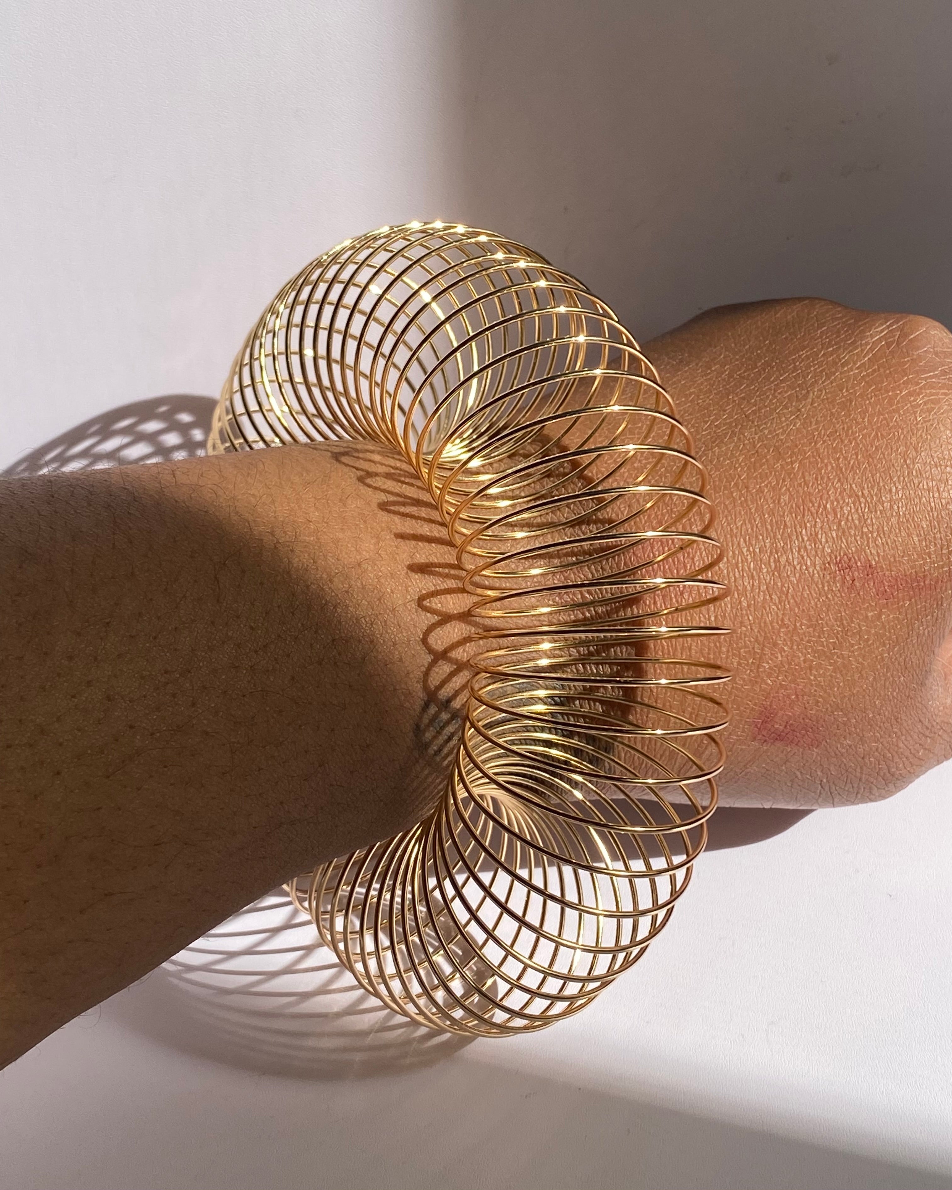 Gold adjustable coil bracelet expanded into bold statement cuff on wrist