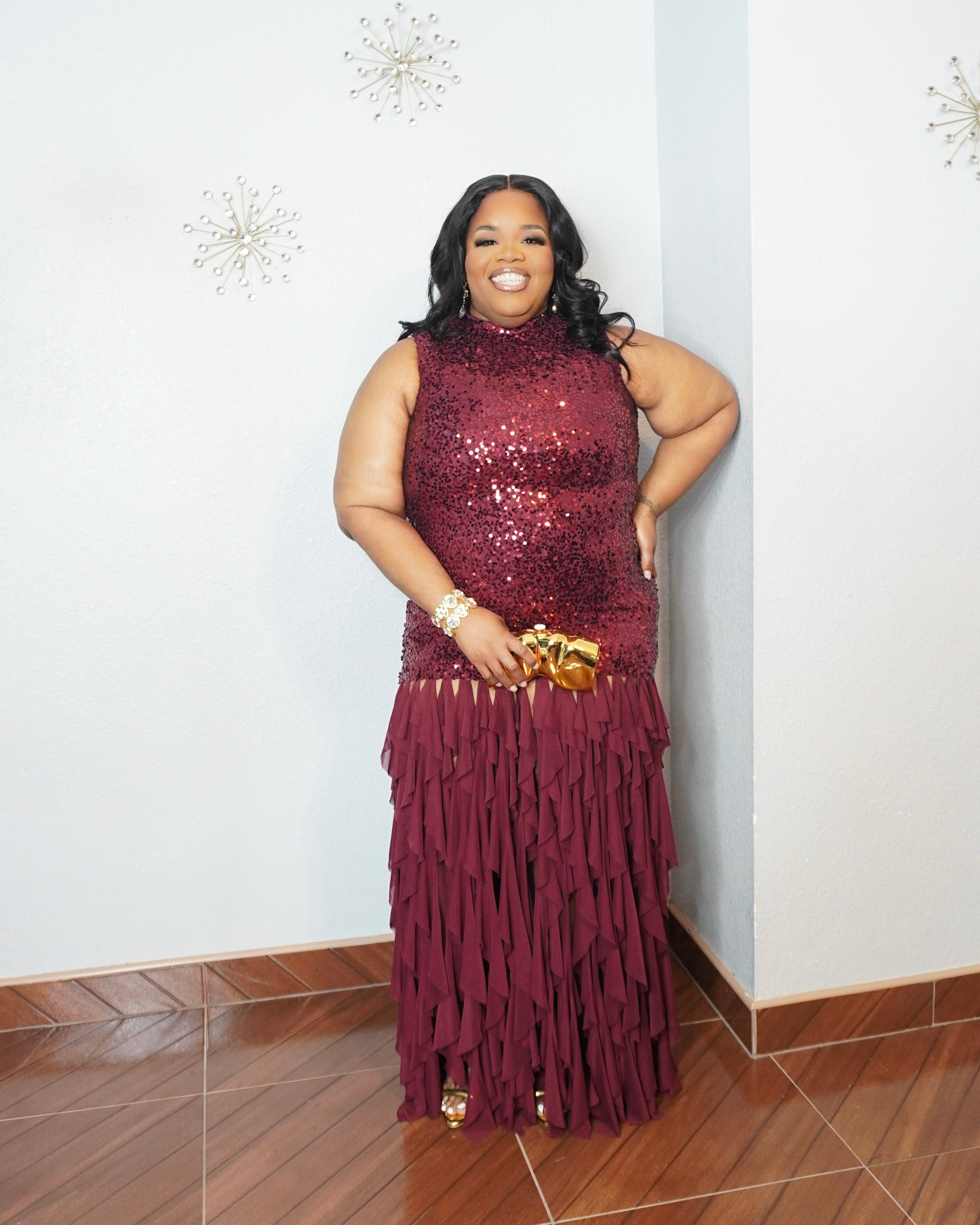 Woman wearing burgundy sequin maxi gown with layered chiffon skirt and gold accessories