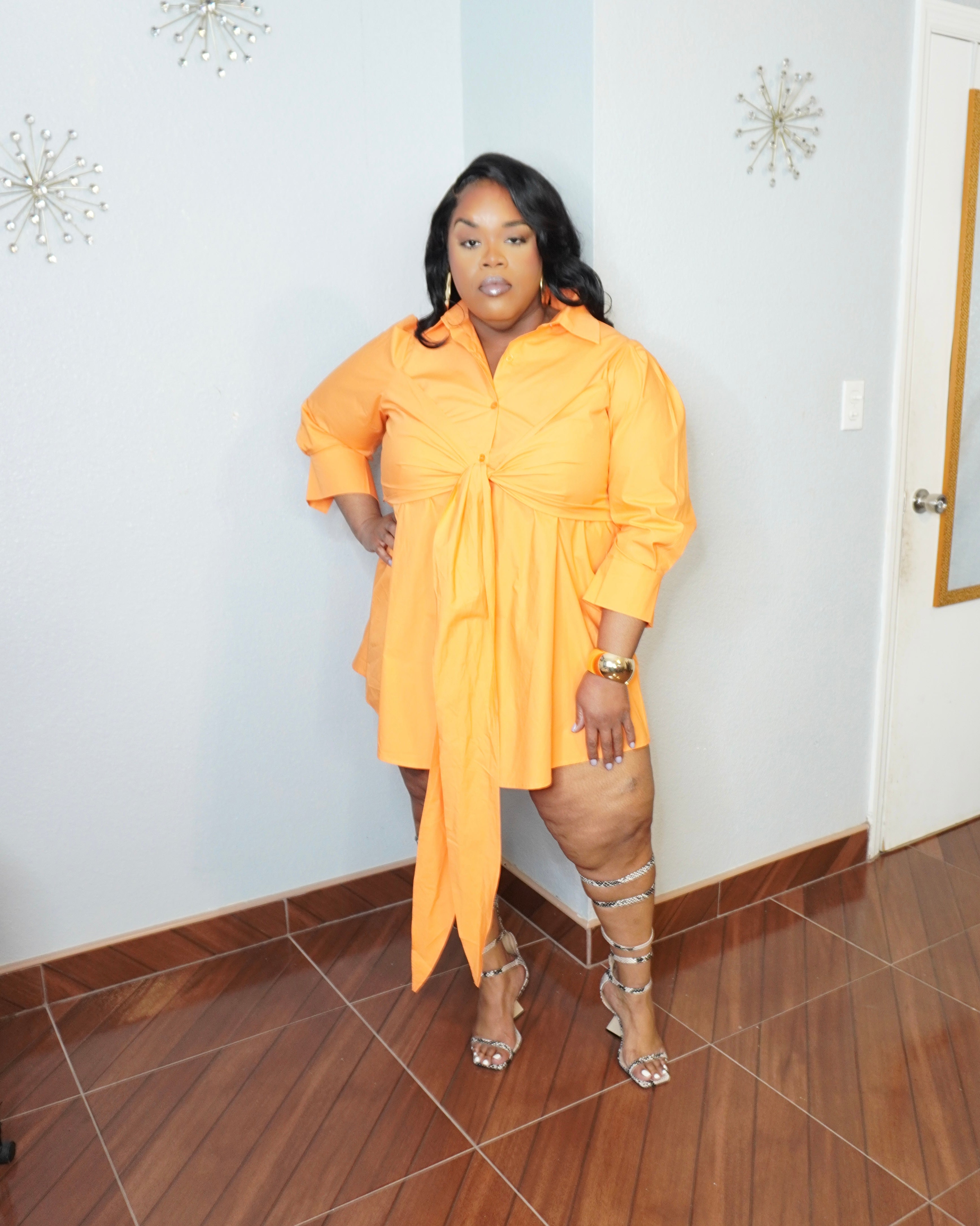 Plus size model posing in orange tie front dress with strappy heels