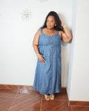 Plus size model wearing a medium wash denim midi dress with adjustable straps, button front detail, smocked back, and side pockets.