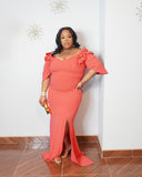 Curvy woman modeling fitted coral formal dress with dramatic shoulder ruffles