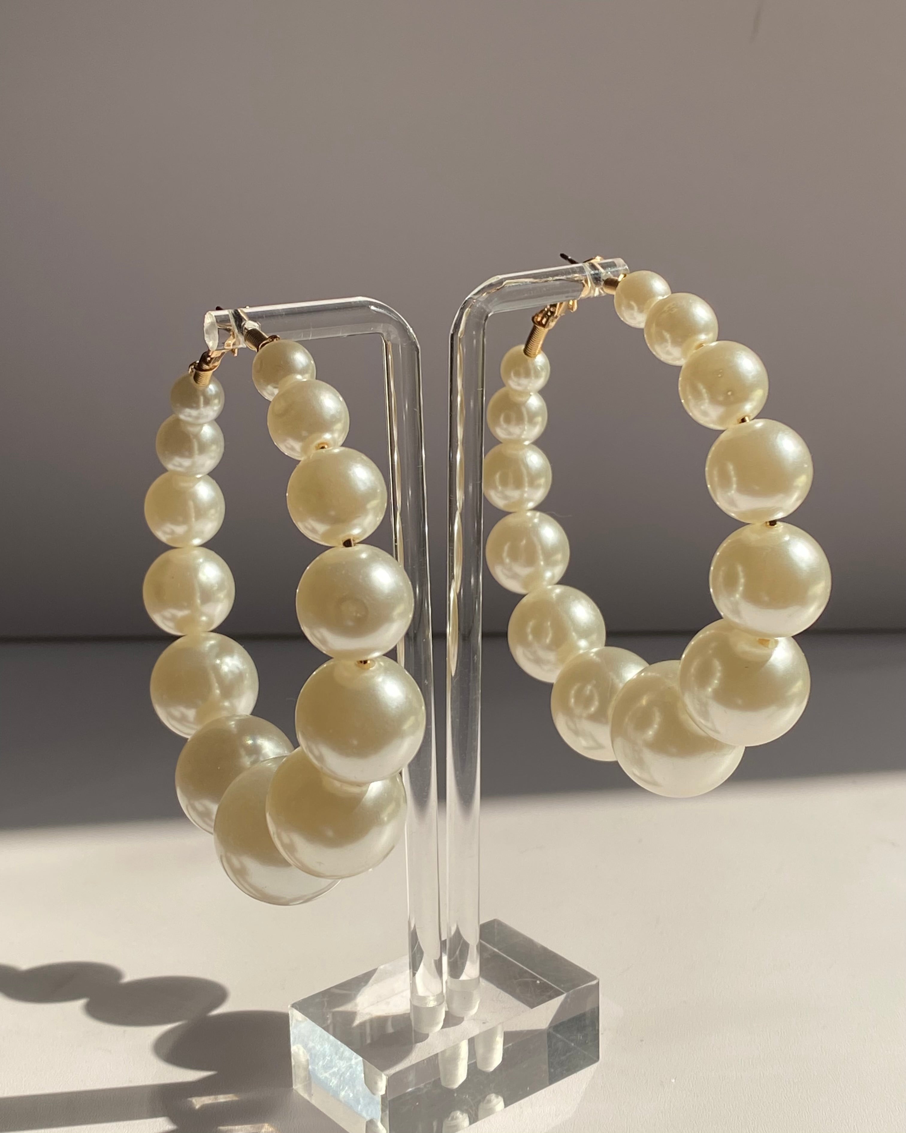 Graduated ivory pearl hoop earrings with gold-tone hardware displayed on a clear acrylic stand.